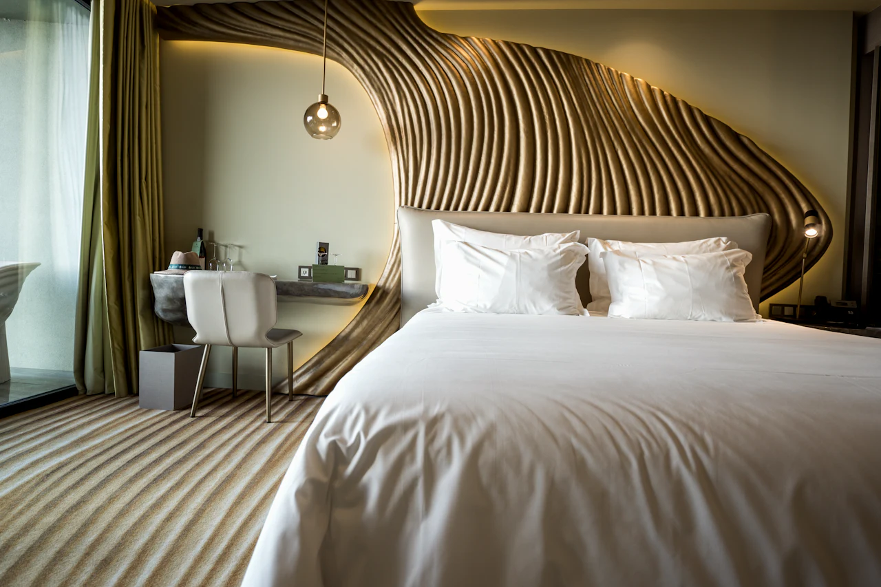 The Corner Room, with a sculptural timber headboard, white linen and a striped rug