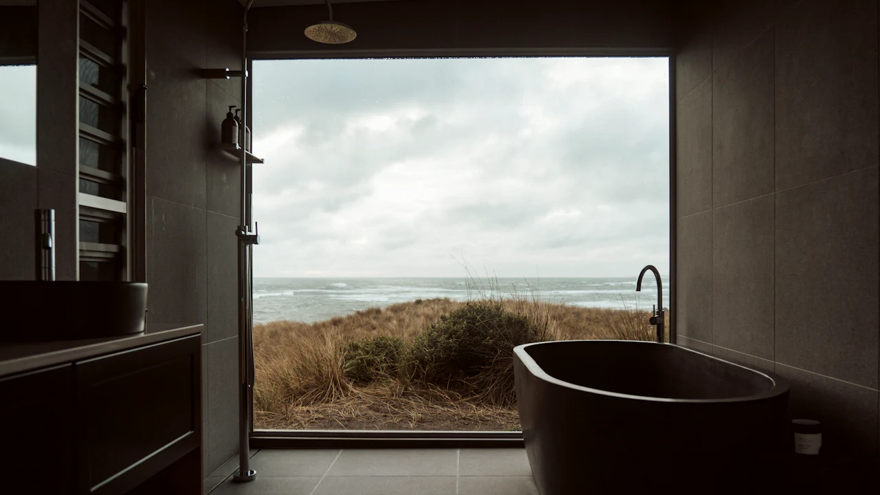 A freestanding stone bath beside a wide window looking out to open landscape