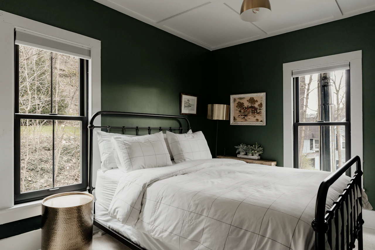 The Alder Suite bedroom, with deep green walls, white bedding and windows onto the trees