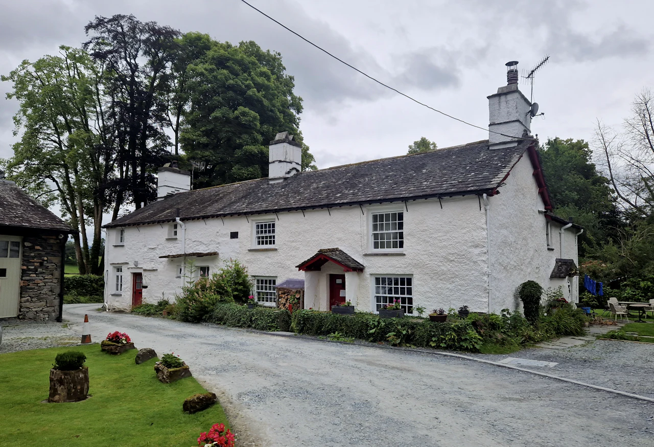 A whitewashed Lakeland cottage with a red door beside a country lane