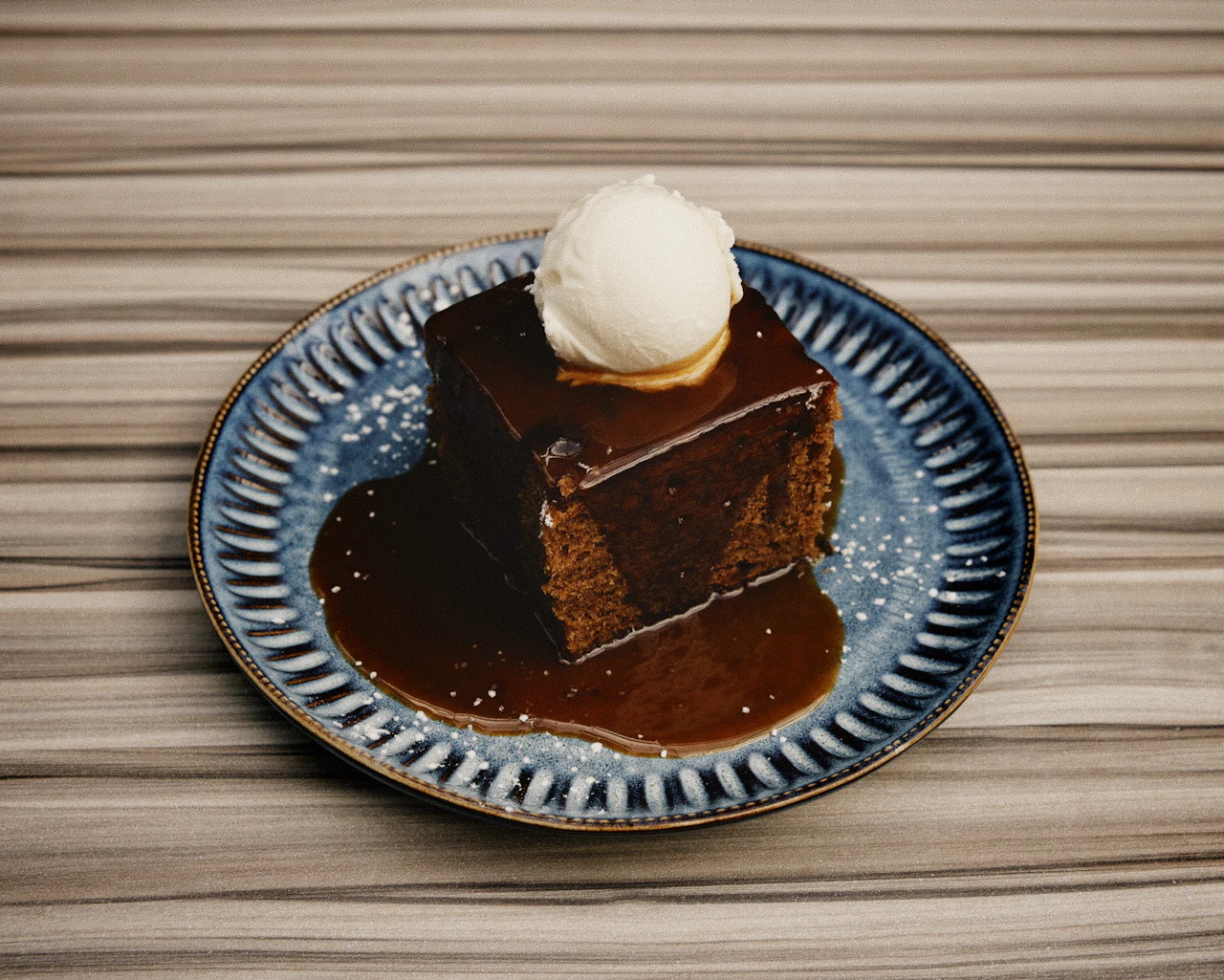 Sticky toffee pudding topped with ice cream, on a blue patterned plate