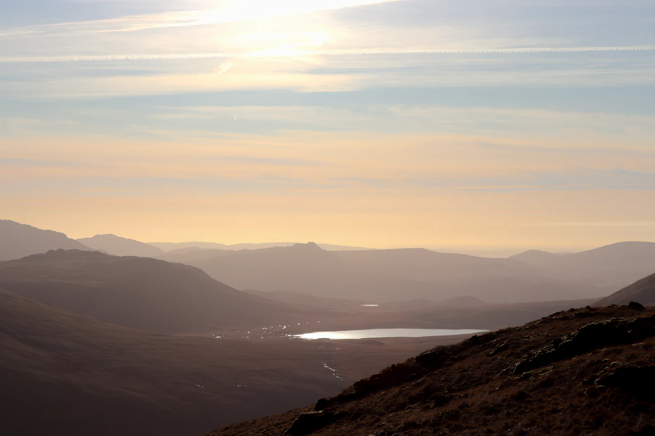 A walker sitting on a hillside high above a Lake District lake