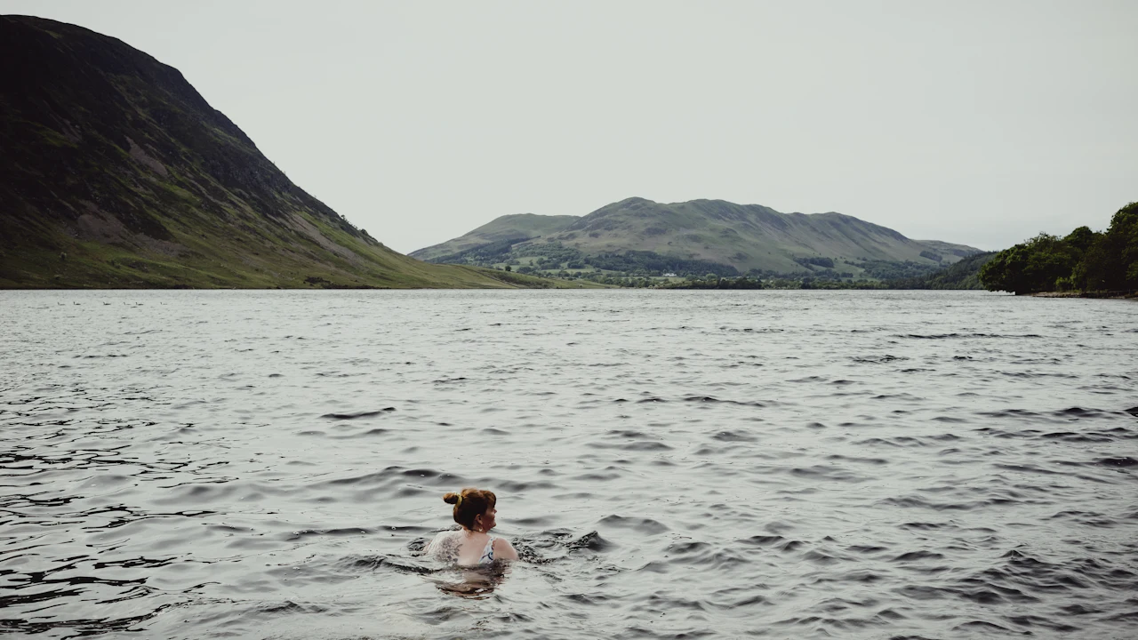 A wild swimmer in a Lake District lake, with fells rising behind